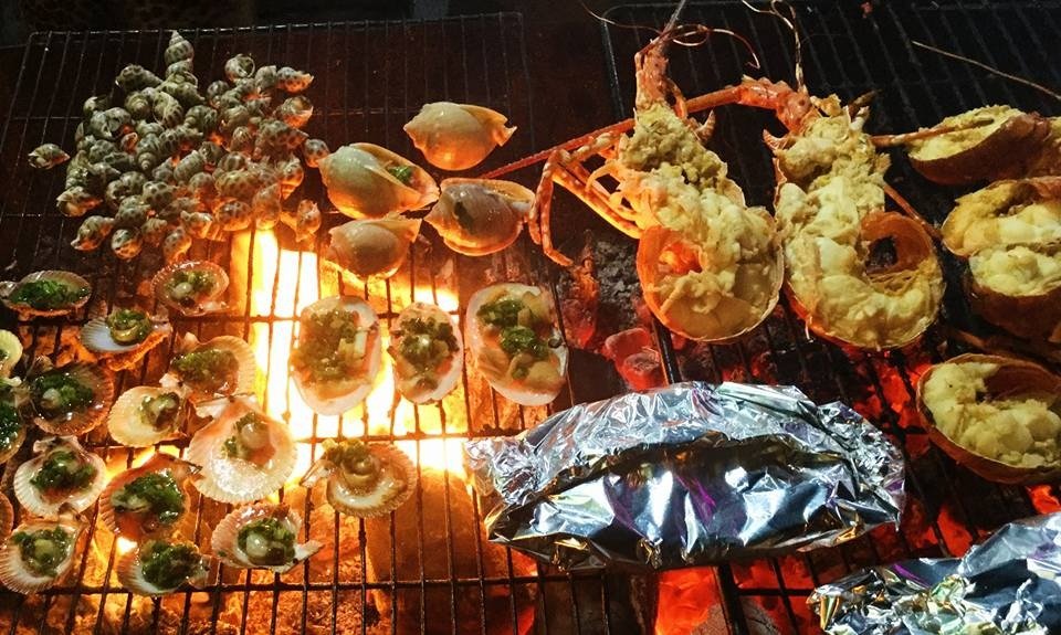 Ẩm thực hải sản nướng tươi ngon trên bếp lửa rực rỡ với tôm hùm, sò điệp, và các loại ốc đẹp mắt.