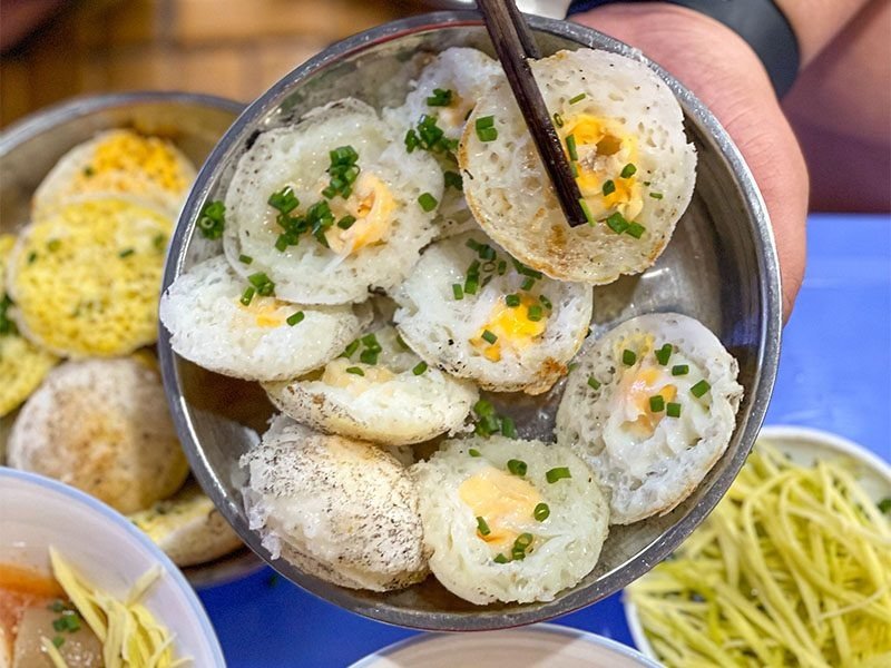 Bánh căn Đà Lạt hấp dẫn với trứng, hành lá xanh tươi và hương vị đặc trưng, được bày trong chén inox.