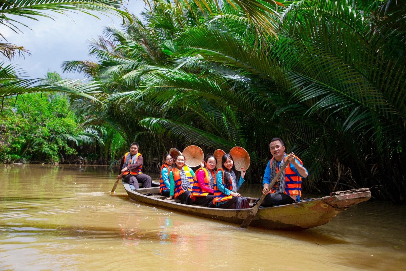 Nhóm người đi thuyền trên sông trong rừng ngập mặn, mặc áo phao và đội nón lá, khám phá vẻ đẹp thiên nhiên Việt Nam.