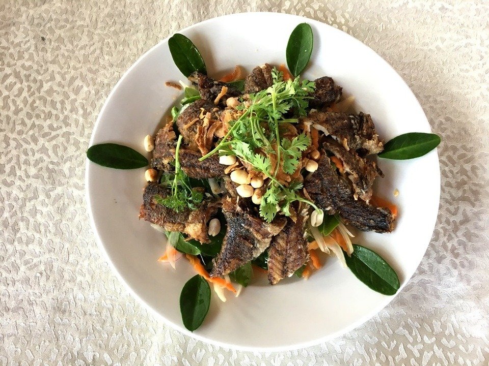 Món ăn hấp dẫn với cá chiên giòn, rau sống, đậu phộng và ngò trên đĩa trắng, bày trí tinh tế và đẹp mắt.