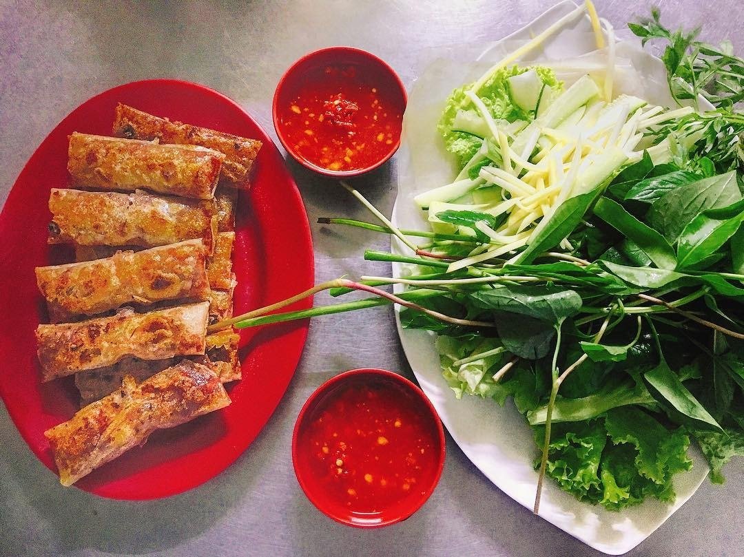 Nem rán giòn vàng bên cạnh các loại rau sống tươi xanh và chén nước chấm đỏ cay ngon hấp dẫn trên bàn.