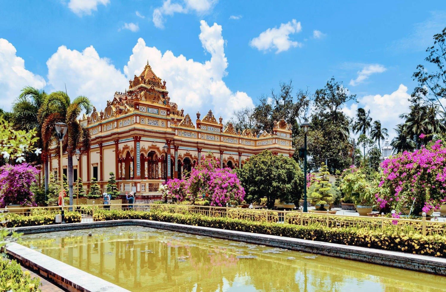 Chùa Vĩnh Tràng, Mỹ Tho với kiến trúc độc đáo, hoa giấy nở rộ và hồ nước trong xanh dưới bầu trời trong xanh.