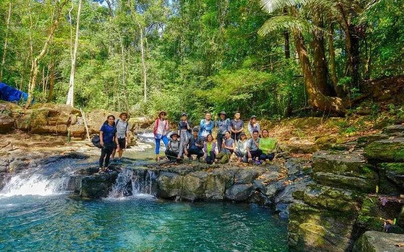 Một nhóm người tận hưởng thời gian thư giãn tại khu rừng nhiệt đới bên dòng suối trong xanh và thác nước.
