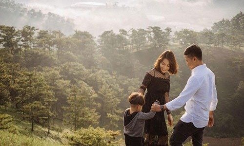 Gia đình hạnh phúc đi dạo trên đồi xanh mướt vào buổi sáng sớm, sương mù nhẹ bao phủ cảnh quan.