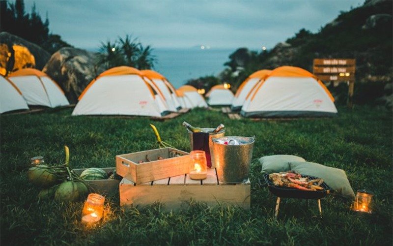 Khu cắm trại buổi tối với các lều trại, nến lung linh, bữa ăn ngoài trời và bầu không khí thư giãn giữa thiên nhiên.