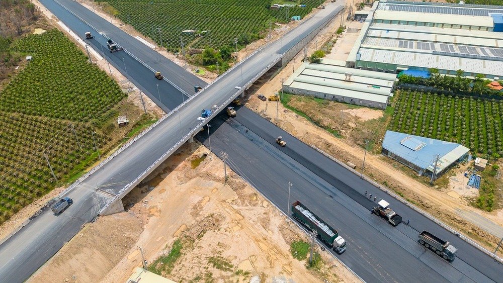 Quang cảnh từ trên cao của dự án xây dựng đường cao tốc và giao lộ với xe cộ và cánh đồng xanh.
