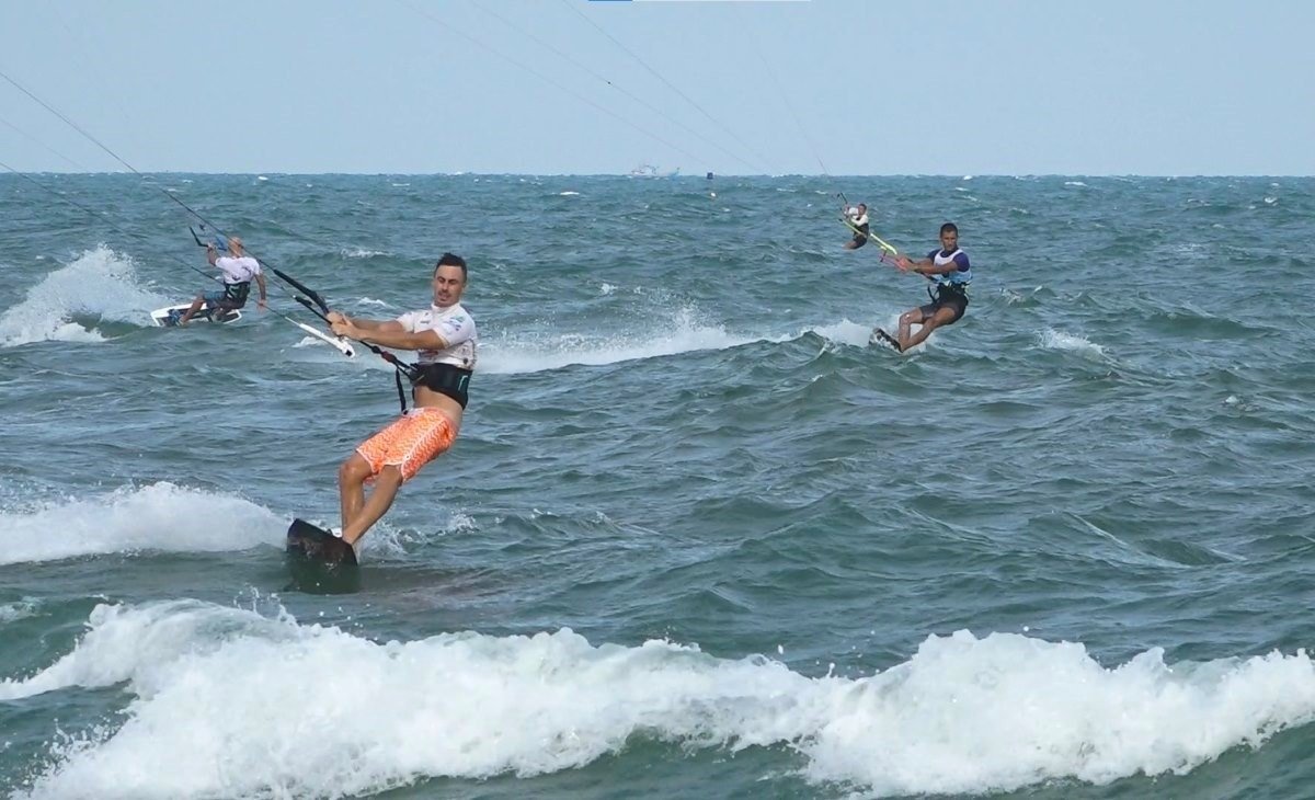 Ba người đàn ông chơi kite surf trên biển đầy sóng, đang điều khiển ván lướt và diều bắt gió mạnh mẽ.