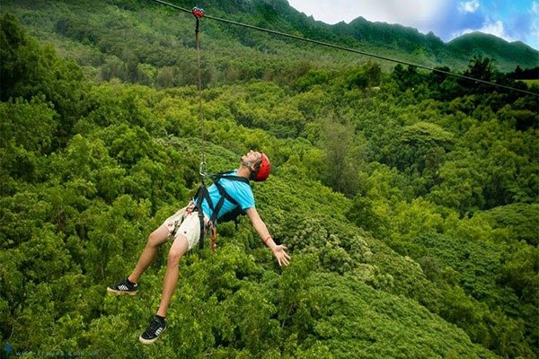 Mô Hình Du Lịch Giải Trí: Xu Hướng Hấp Dẫn Khách Du Lịch Hiện Đại 2 Người đàn ông vui vẻ trượt zipline qua khu rừng xanh mướt, mặc áo xanh và đội nón bảo hiểm đỏ, cảm giác phấn khích.