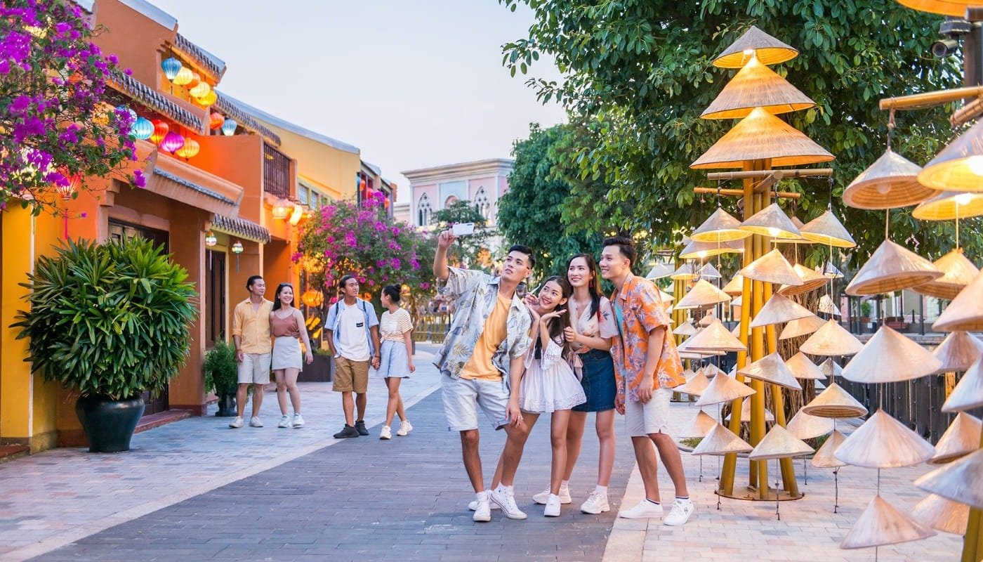 Nhóm bạn trẻ chụp ảnh selfie tại phố đi bộ, bao quanh bởi lồng đèn và nón lá trang trí, không khí vui tươi và sôi động.
