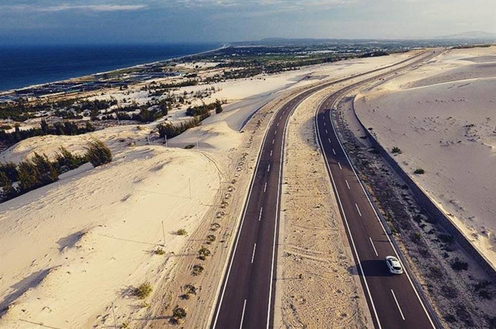 Con đường nhựa dài uốn lượn giữa sa mạc cát trắng và biển xanh, tạo nên cảnh quan thiên nhiên đẹp mắt.
