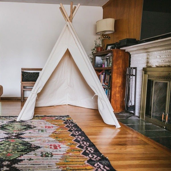 Bí Quyết Cắm Trại Tại Nhà: Trải Nghiệm Chill Như Đi Dã Ngoại 2 Lều vải trắng dựng trong phòng khách ấm cúng, gần lò sưởi và tủ sách gỗ, trải thảm hoa văn bắt mắt.