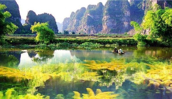 Phong cảnh thiên nhiên tuyệt đẹp với dòng sông trong xanh, cây cối tươi tốt và núi đá vôi hùng vĩ ở đằng xa.