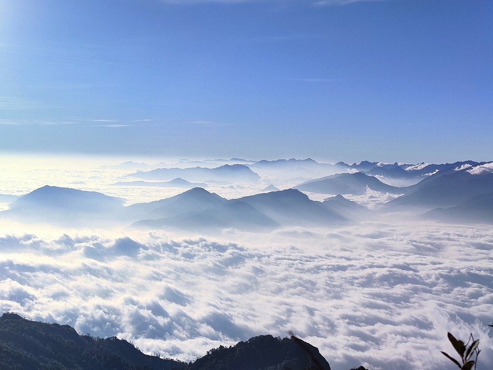 Phong cảnh tuyệt đẹp của dãy núi được bao quanh bởi mây trắng mịn và bầu trời xanh trong, tạo cảm giác yên bình.