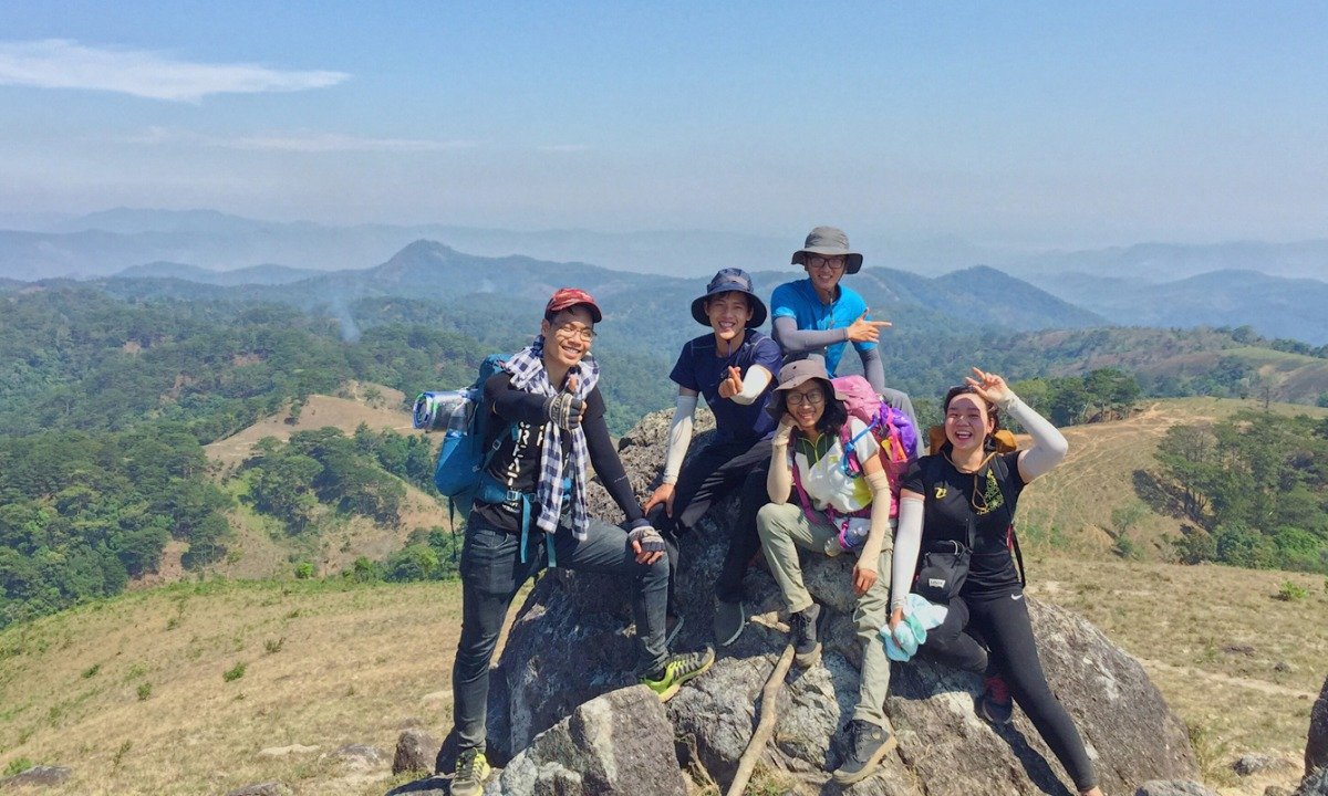 Đi Tour Trekking Tà Năng Phan Dũng: Mùa Nào Đẹp Nhất Trong Năm? 2 Một nhóm người vui vẻ trên đỉnh núi với phong cảnh thiên nhiên tuyệt đẹp, không gian xanh lá và núi non bát ngát.