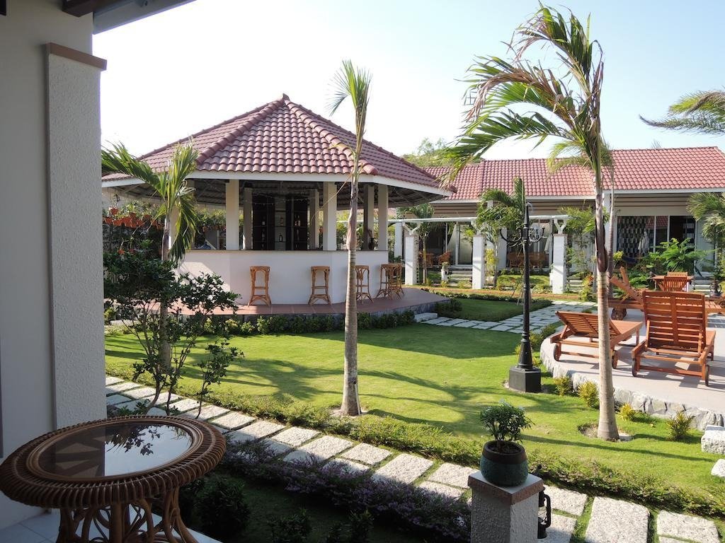 Khu vườn sang trọng với nhà chòi mái ngói, cây cối xanh mướt, ghế ngồi thoải mái và lối đi lát đá. Không gian thư giãn lý tưởng.