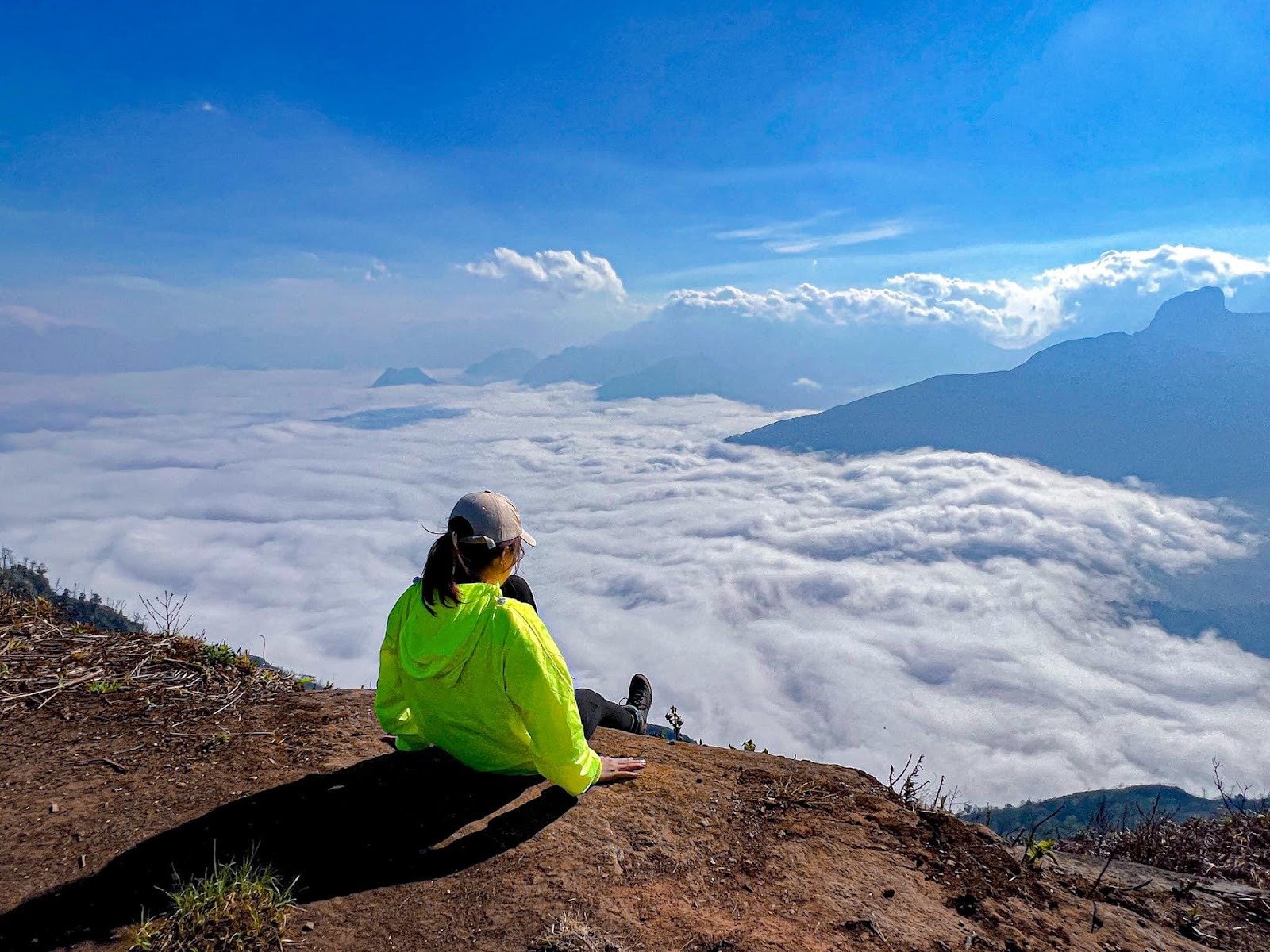 Người phụ nữ ngồi trên vách đá, ngắm nhìn biển mây dưới bầu trời xanh tại một địa điểm du lịch nổi tiếng trên núi.