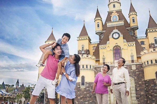 Gia đình hạnh phúc vui chơi ở khu vui chơi giải trí nổi tiếng, với lâu đài phía sau và nền trời xanh tươi sáng.