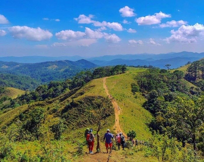 Nhóm người leo núi trekking trên đồi cỏ xanh mướt vào một ngày nắng đẹp tại địa danh du lịch hoang sơ.