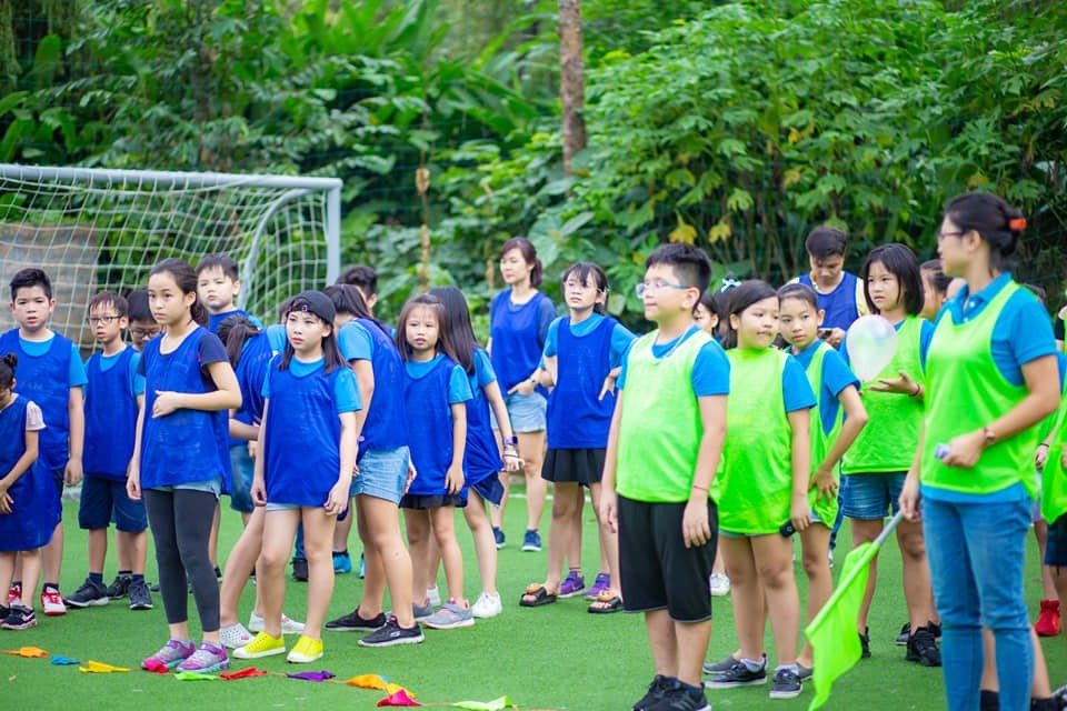 Team Building Học Sinh: Chìa Khóa Phát Triển Kỹ Năng Mềm Quan Trọng 4 Nhóm trẻ em tham gia hoạt động thể thao ngoài trời, mặc áo xanh và vàng, có khung thành và cây xanh xung quanh.