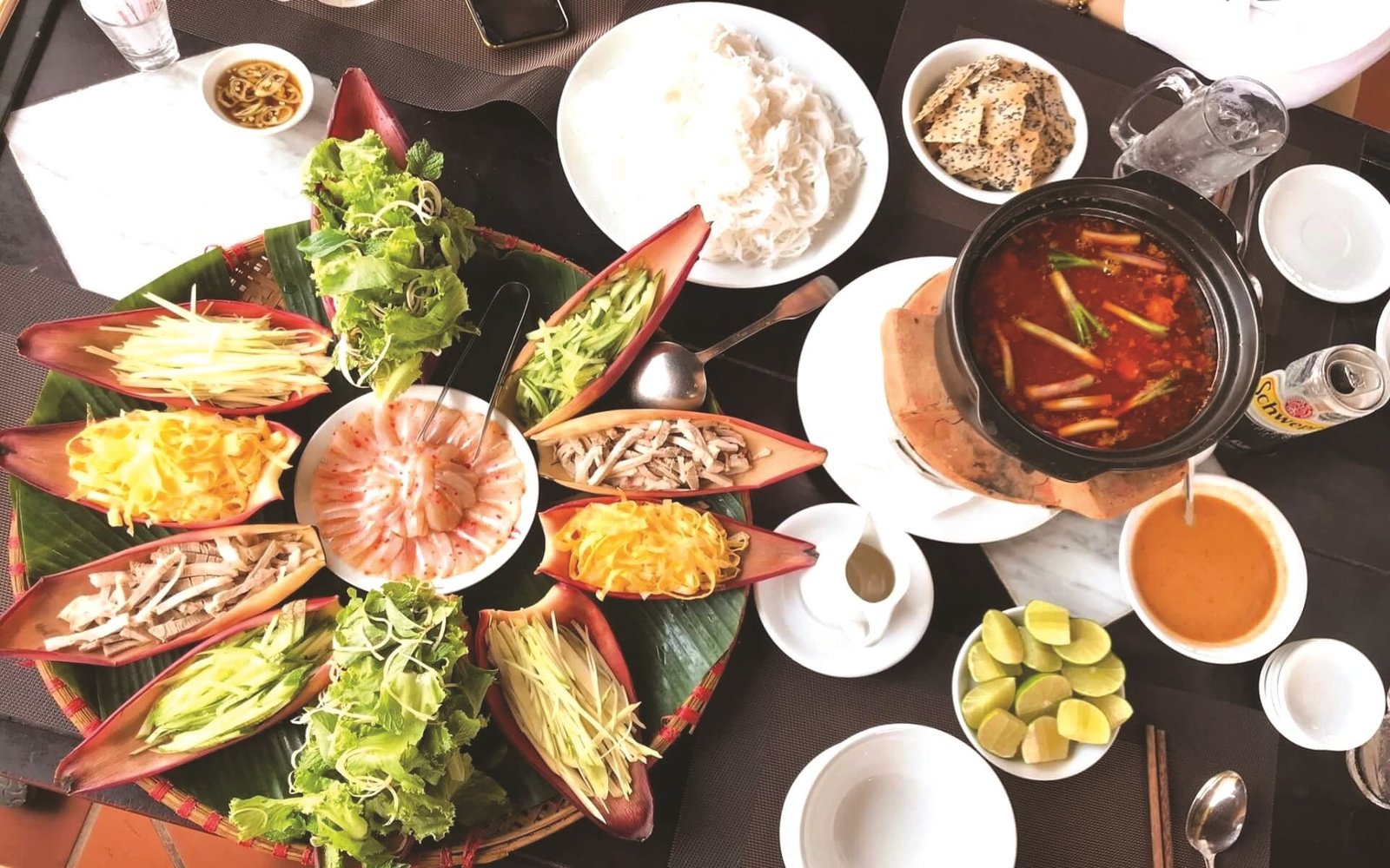 Một bữa ăn truyền thống Việt Nam với nhiều loại rau, thịt, tôm bày biện đẹp mắt và nồi súp nóng hổi đầy màu sắc.