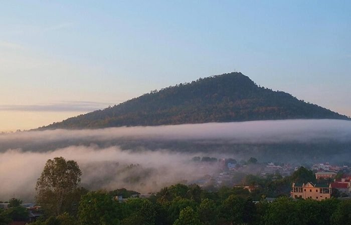 Cảnh đẹp núi Bà Đen Tây Ninh bao phủ trong sương mù mờ ảo, với làng mạc và cây cối xanh tươi phía dưới.