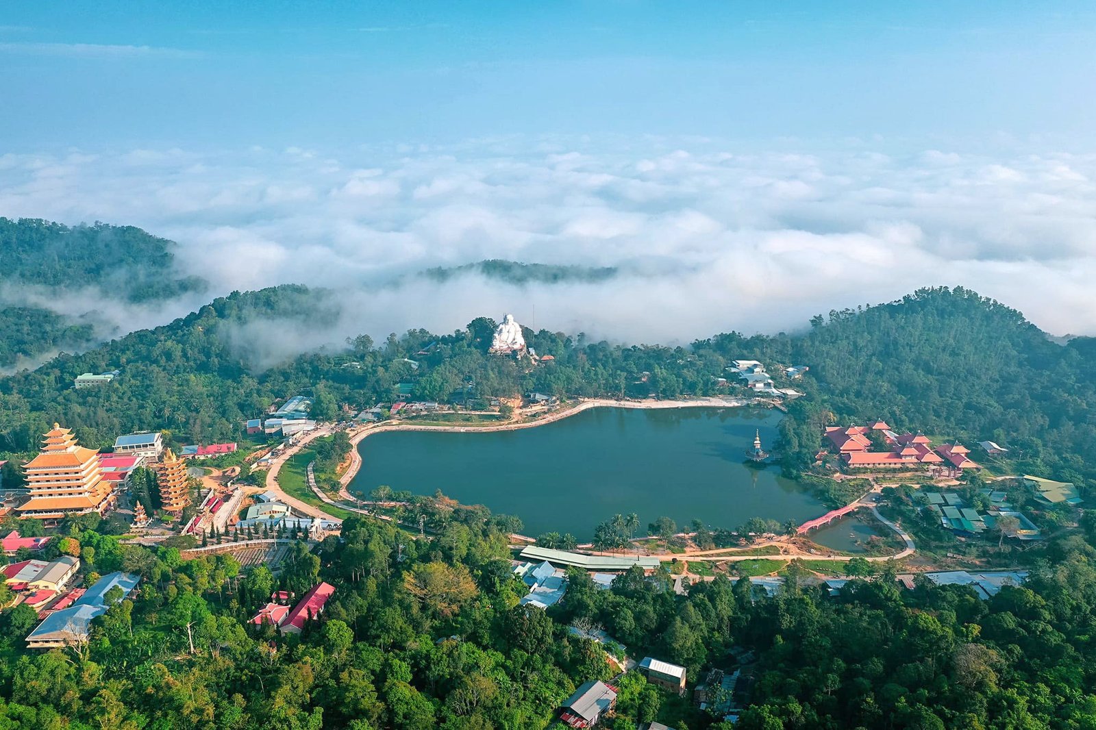 Khung cảnh núi rừng xanh mát với hồ nước lớn, bao quanh là các công trình kiến trúc nổi bật, bầu trời mây phủ.