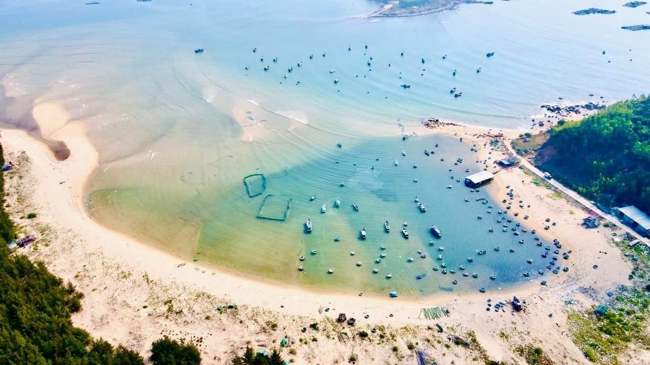 Ảnh chụp từ trên cao của một khu vực bãi biển với nhiều tàu thuyền neo đậu và nước biển trong xanh.