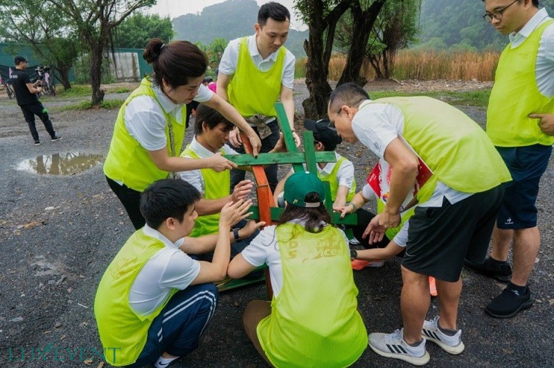 Nhóm người mặc áo khoác vàng đang hợp tác thực hiện một nhiệm vụ đội nhóm ngoài trời tại công viên cây xanh.