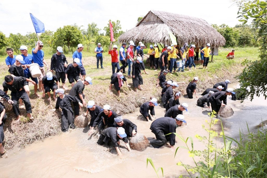 Người dân tham gia hoạt động lễ hội bắt cá trong con mương trò chơi dân gian gần các ngôi nhà tranh ở vùng đồng quê.