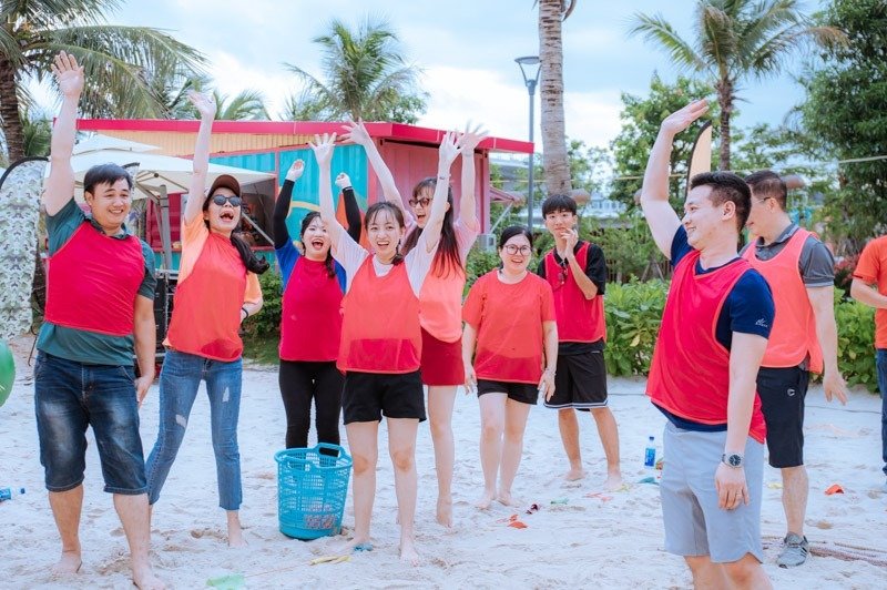 Team Building Vũng Tàu: Trải Nghiệm Thú Vị Tại Thành Phố Biển Tuyệt Đẹp 2 Nhóm người vui vẻ tham gia hoạt động teambuilding tại bãi biển với trang phục áo đồng phục màu đỏ, năng động và hào hứng.