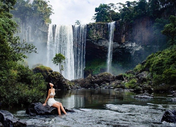 Người phụ nữ thư giãn bên dòng thác Ma Gai - Dam Bri hùng vĩ giữa thiên nhiên kỳ dịu với cây xanh bao quanh ở Tây Nguyên, Việt Nam.