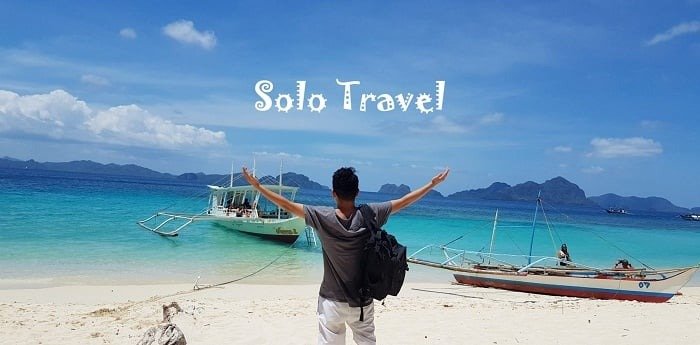 Du khách đứng trên bãi biển hoang sơ, vươn tay đón biển xanh và thuyền nhỏ, chữ Solo Travel nổi bật trên trời.