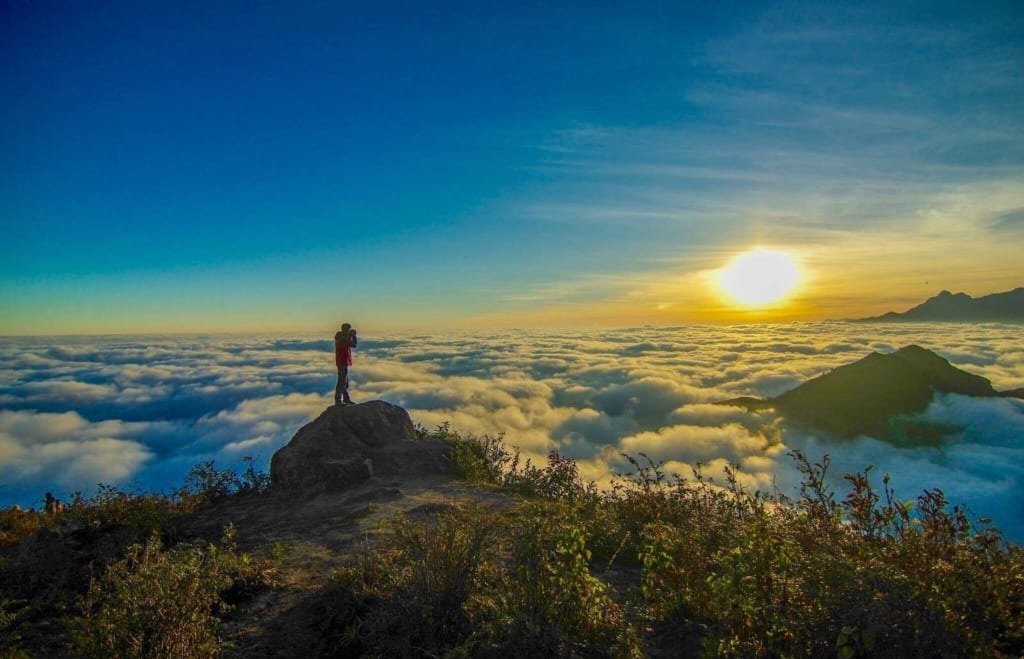 Người đàn ông đứng trên đỉnh núi nhìn ngắm hoàng hôn tuyệt đẹp trên biển mây giữa không gian thiên nhiên kỳ vĩ.