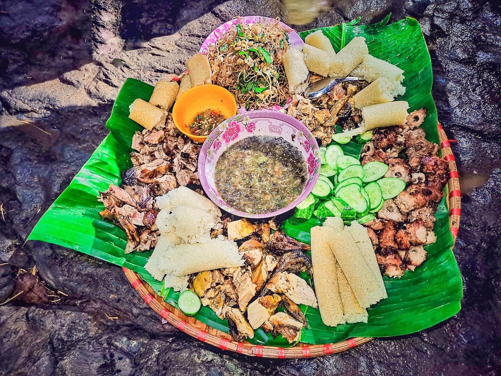 Mâm cơm Việt Nam truyền thống với thịt nướng, cơm lam, rau sống, và bún vào bát tô lớn trên lá chuối xanh tươi.