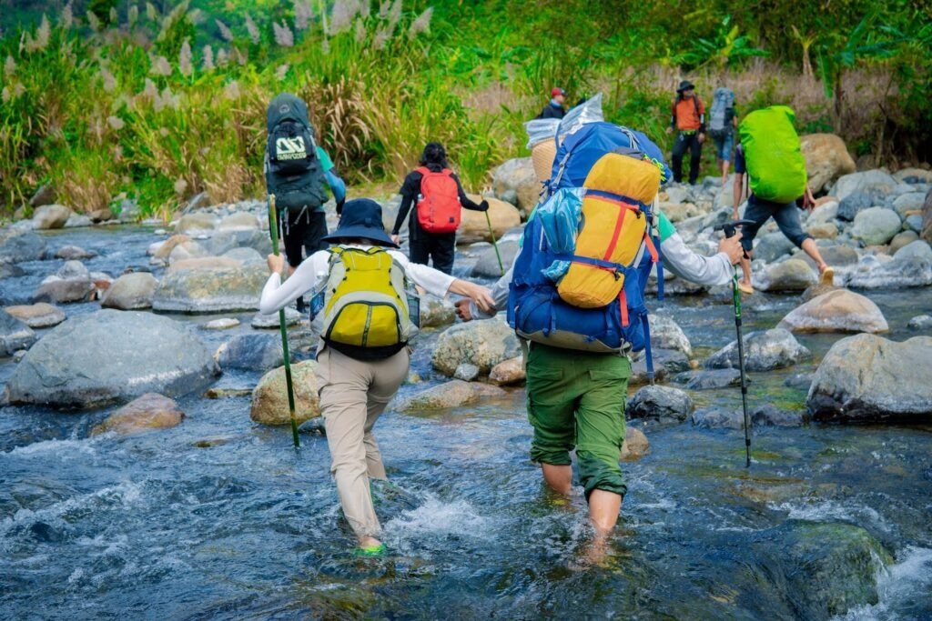 Nhóm người mạo hiểm băng qua dòng suối với những ba lô lớn trong hành trình leo núi và khám phá thiên nhiên hoang dã.