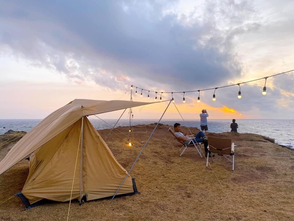 Mẹo Dựng Lều Nhanh Chóng Khi Đi Trekking: Hướng Dẫn Chi Tiết 4 Cắm trại trên bờ biển với lều, ghế thư giãn và hoàng hôn huyền ảo, ánh đèn lung linh giữa trời xanh dịu dàng.