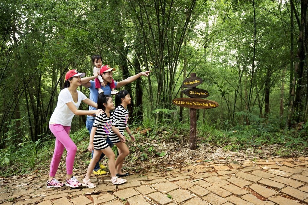 Gia đình háo hức thăm quan thiên nhiên, chỉ tay về phía trước gần biển báo trong rừng xanh đậm chất phiêu lưu.