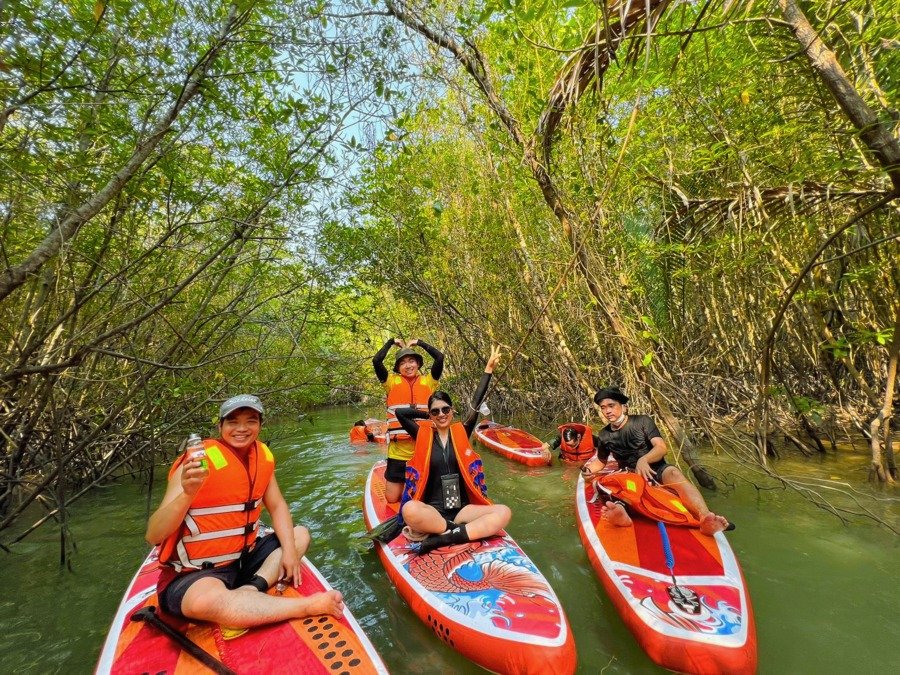 Nhóm người chèo thuyền đứng khám phá khu rừng ngập mặn xanh tươi vào một ngày nắng đẹp, tạo dáng vui vẻ.