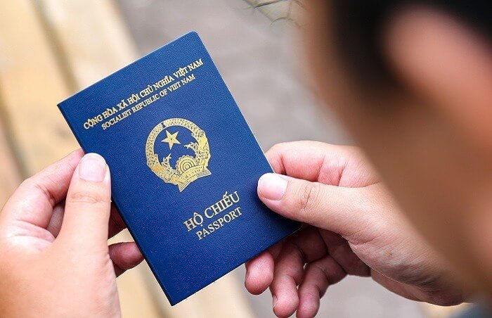 Người cầm hộ chiếu Việt Nam màu xanh đậm, biểu tượng quốc huy nổi bật, đang chuẩn bị đi du lịch quốc tế.