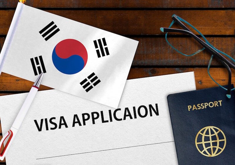 Hồ sơ xin visa Hàn Quốc với hộ chiếu, bút và cờ Hàn Quốc trên nền gỗ. Quy trình làm visa nhanh chóng.