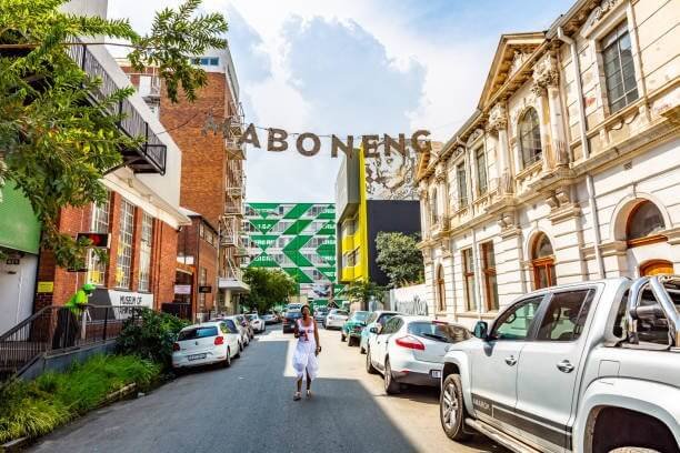 Kinh Nghiệm Du lịch Johannesburg: Thành Phố Bậc Nhất Của Nam Phi 4 Khu phố Maboneng sầm uất với kiến trúc độc đáo, xe đỗ hai bên đường, và ánh nắng rực rỡ chiếu sáng cảnh quan.