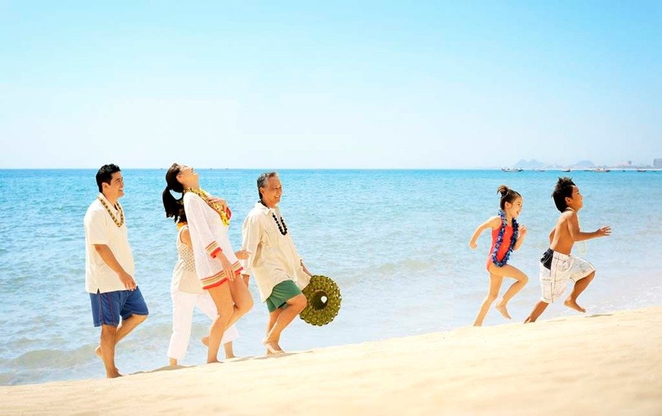 Gia đình vui vẻ đi dạo trên bãi biển nắng, sóng biển xanh trong tạo nên khung cảnh thư giãn và hạnh phúc.