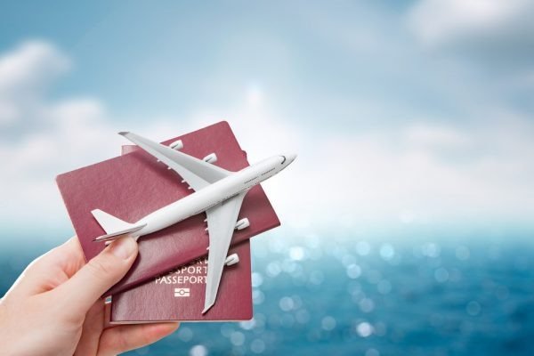 Top 5 Kinh Nghiệm Du Lịch Biển Cho Chuyến Đi Hoàn Hảo 3 Mô hình máy bay trên tay cầm hai hộ chiếu, nền là bầu trời xanh và nước biển, biểu tượng du lịch quốc tế.