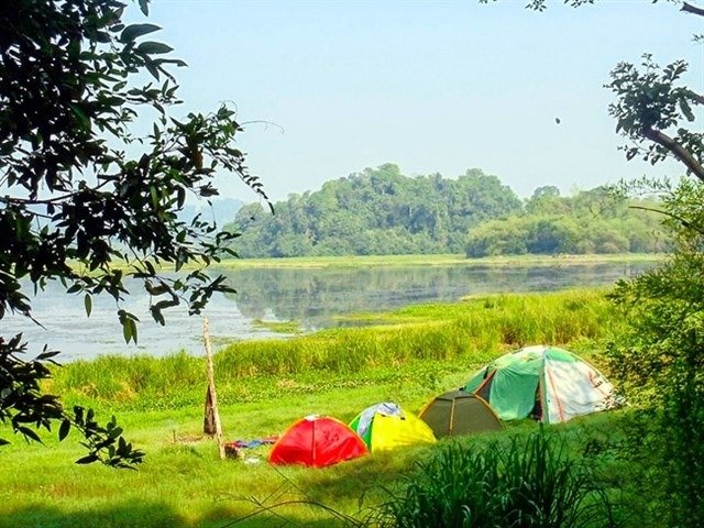 Cắm Trại Nam Cát Tiên: Trải Nghiệm Mới Lạ Và Đầy Thú Vị Chờ Đón Bạn 2 Khu cắm trại ven hồ với lều màu sắc rực rỡ, bao quanh bởi cây xanh, nền phong cảnh thiên nhiên tuyệt đẹp.