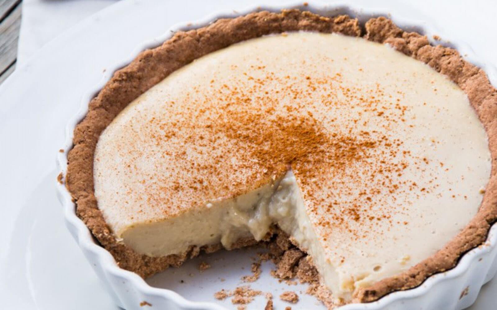 Điểm danh 7 món ăn đặc sắc của ẩm thực Nam Phi 4 Bánh tart kem mềm thơm, phủ bột quế, đã cắt một miếng, trên đĩa sứ trắng. Bánh hấp dẫn cho bữa tráng miệng.