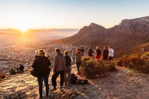 Du lịch Cape Town – Khám phá thành phố đẹp nhất Nam Phi 2 Một nhóm du khách ngắm hoàng hôn từ đỉnh núi, nhìn xuống khung cảnh thành phố tuyệt đẹp và núi đồi xanh biếc.