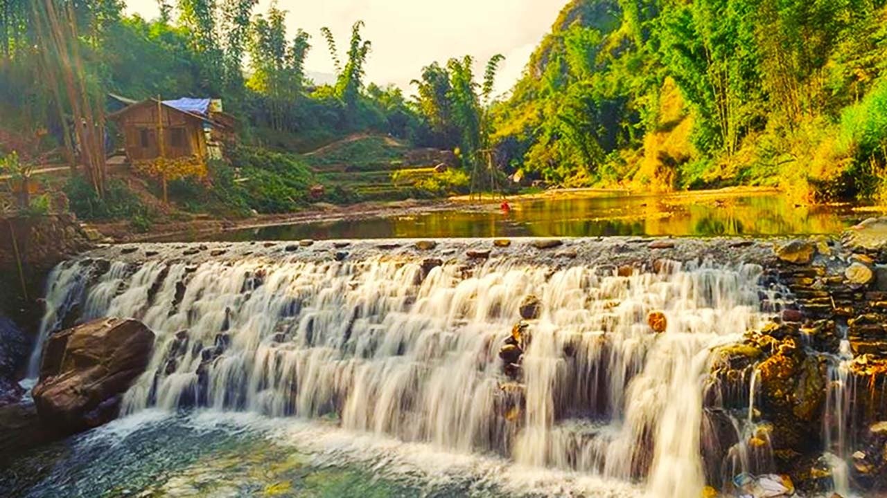 Cắm Trại Nam Cát Tiên: Trải Nghiệm Mới Lạ Và Đầy Thú Vị Chờ Đón Bạn 3 Thác nước nhỏ chảy róc rách qua ghềnh đá, cạnh ngôi nhà gỗ và rừng cây xanh tươi vào ngày nắng đẹp.