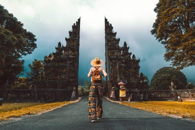 Khách du lịch đi qua cổng cổ truyền thống tại Bali, Indonesia, xung quanh là cảnh đẹp thiên nhiên xanh tươi.