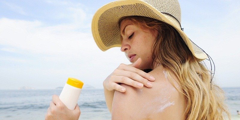 Top 5 Kinh Nghiệm Du Lịch Biển Cho Chuyến Đi Hoàn Hảo 4 Người phụ nữ đội mũ rộng vành thoa kem chống nắng trên vai tại bãi biển, bảo vệ da dưới ánh nắng mặt trời mùa hè.