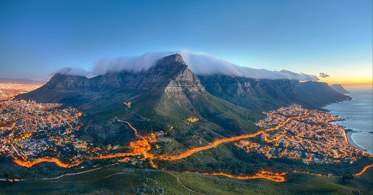 Phong cảnh ngoạn mục của núi Table ở Cape Town với lớp mây phủ đỉnh, ánh đèn thành phố lấp lánh về đêm.